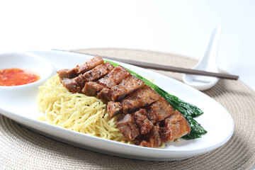 cook dry egg noodle mee with grilled chicken chop, pork cutlet and vegetable in soy chilli sauce in plate chopstick on brown cloth white table asian chef cuisine halal food menu for restaurant