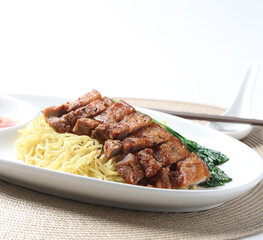 cook dry egg noodle mee with grilled chicken chop, pork cutlet and vegetable in soy chilli sauce in plate chopstick on brown cloth white table asian chef cuisine halal food menu for restaurant