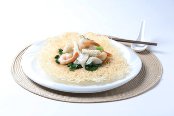 deep fried crispy bee hoon noodle with mixed seafood fish, prawn, squid, octopus and vegetables in thick gravy egg sauce on brown cloth white table asian chef cuisine halal food menu for restaurant