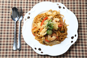 stir fried Malay spicy chilli noodle mamak mee goreng with mixed seafood fish, prawn, squid, meat and lime in plate on white background asian chef cuisine halal food menu for cafe