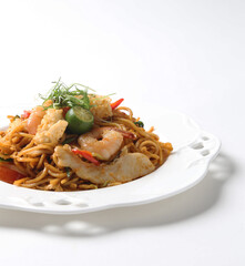 stir fried Malay spicy chilli noodle mamak mee goreng with mixed seafood fish, prawn, squid, meat and lime in plate on white background asian chef cuisine halal food menu for cafe