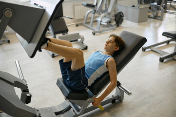 Fototapeta na wymiar Preteen boy training legs on sports equipment at gym