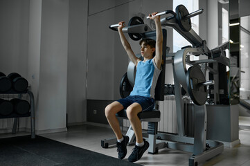 Naklejka na ściany i meble Teenager boy training arms, chest, shoulders and back on exercise machine