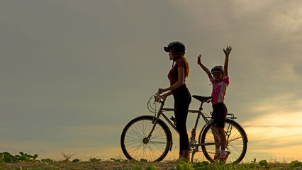Silhouette biker lovely family at sunset over the ocean.  Mom and daughter bicycling happy and relax on the beach.  Lifestyle and Family Concept.