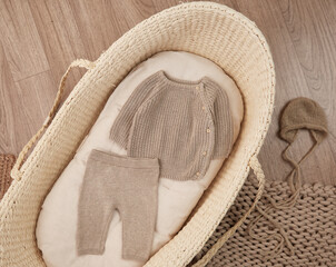 knitted natural newborn outfit top and pants in a moses basket against a wooden floor 