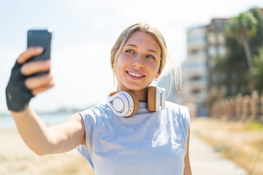 Young blonde woman at outdoors wearing sport wear and taking a selfie with the mobile