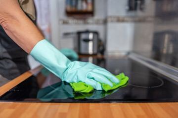 Hand of woman with gloves scrubbing the ceramic hob with a cloth and soap.