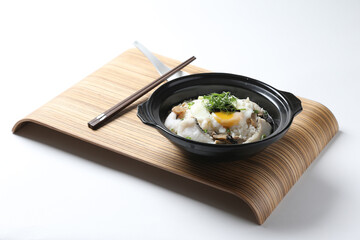 Hong Kong congee porridge rice with seafood fish, prawn, squid, mushroom, egg and vegetables in black hot clay pot on wood tray white background asian chef halal food restaurant banquet cafe menu