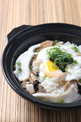 Hong Kong congee porridge rice with seafood fish, prawn, squid, mushroom, egg and vegetables in black hot clay pot on wood tray white background asian chef halal food restaurant banquet cafe menu
