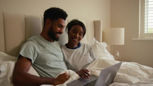 Couple at home in bed looking at laptop computer together - shot in slow motion
