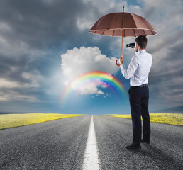 Businessman cover himself with an umbrella and watches far with a binocular