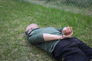 Arrested man in handcuffs face down in the grass of a park.