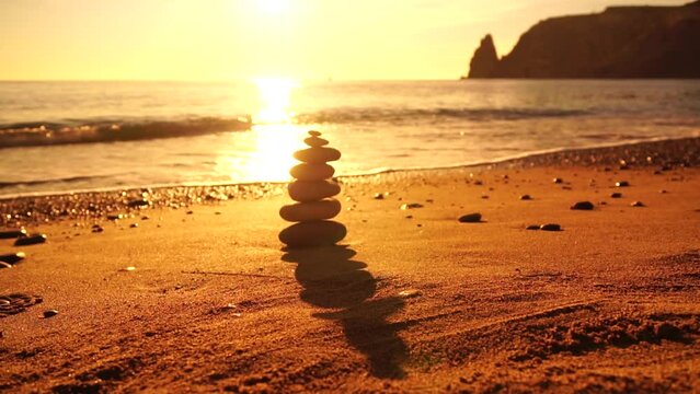 Balanced rock pyramid on pebbles beach, sunny day and clear sky at sunset. Golden sea bokeh on background. Selective focus, zen stones on sea beach, meditation, spa, harmony, calm, balance concept.