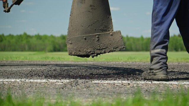 Man patching road. Road surface repair. Pothole asphalt road repairs. Roadway repair. Close-up in 4K, UHD