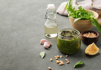 Traditional Italian pesto in a jar with green basil, pine nuts, cheese and olive oil on a green...