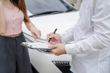 Insurance agent writing on clipboard while examining car after accident claim being assessed and...