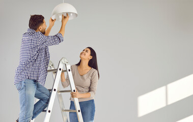 Happy loving couple changing light bulb in new apartment. Family moving in new house, doing DIY...