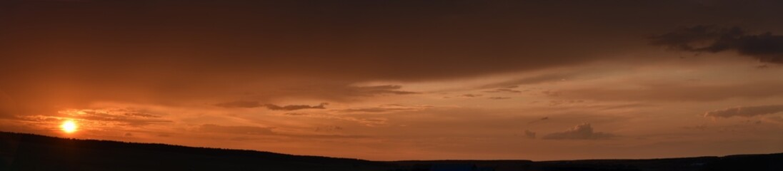 Panorama of a sunset evening with pink clouds and the sun. Beautiful evening clouds.