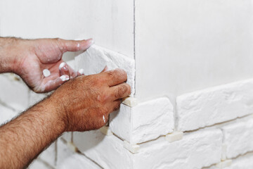 A man glues a white decorative stone in the form of a brick to the wall. Decor element, copy space for text