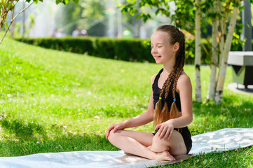 Naklejka na ściany i meble Girl schoolgirl sits in the lotus position in the park.