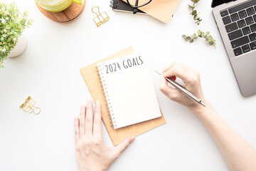 Woman is writing 2024 goals for new year resolutions plan.