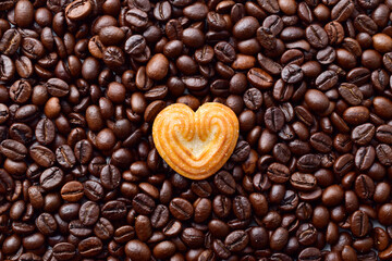 Top view of heart shape biscuit on roasted coffee beans