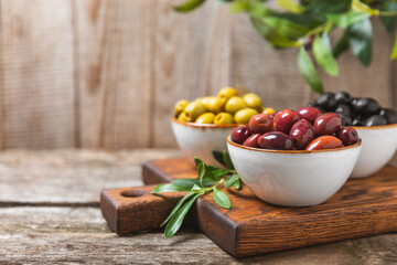 Green, black and red olives, olive oil on a brown wooden background. Fresh juicy olives in a bowl and fresh olive leaves. Vegan. Olive fruits. Place for text. Copy space.