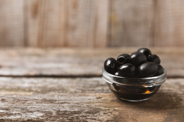 Black olives, olive oil on a brown wooden background. Fresh juicy olives in a bowl and fresh olive leaves. Vegan. Olive fruits. Place for text. Copy space.