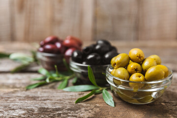 Green, black and red olives, olive oil on a brown wooden background. Fresh juicy olives in a bowl and fresh olive leaves. Vegan. Olive fruits. Place for text. Copy space.