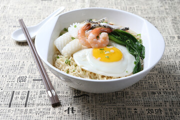 cook Japanese instant noodle mee soup with seafood fish, prawn, octopus, fried egg and vegetables on bowl chopstick on white vintage newspaper background asian chef halal food restaurant banquet menu