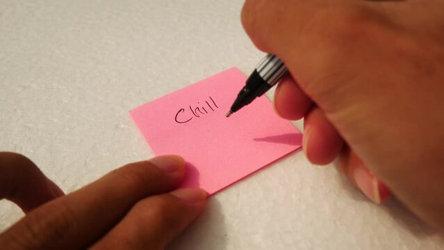 Man writing "CHILL OUT" on a pink notepaper with a black pen.