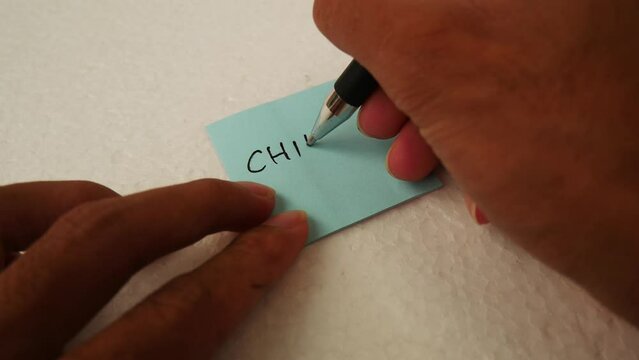 Man writing "CHILL" on a blue notepaper with a black pen.