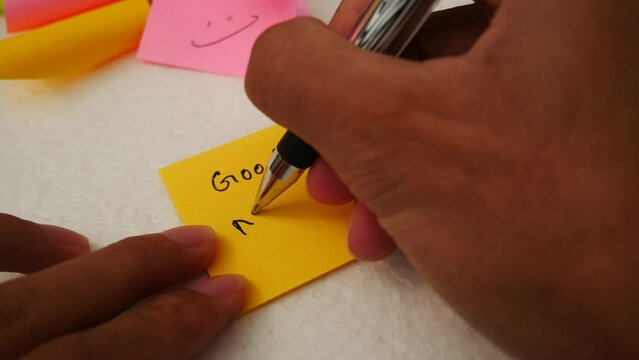 Male hand writing the phrase "Good morning" on a yellow of note pap