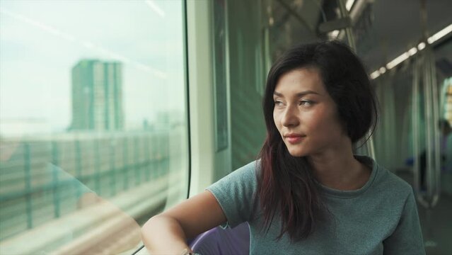 A close shot of a beautiful Indian young stressed woman solo traveler in a traditional salwar kurta sitting in a moving metro train leaning on a window and looking outside. Mental health concept