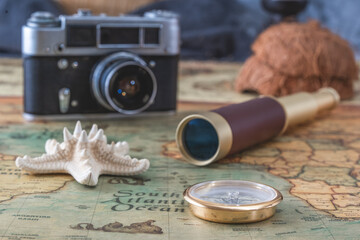brass compass, a spyglass and a starfish lie on an old map against the background of a vintage film camera