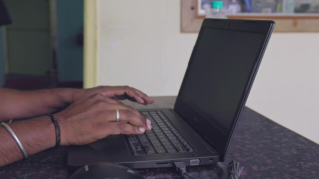 Close-up of a man sitting at a table in a house, typing on a laptop keyboard