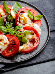 Plate of healthy classic caprese salad with ripe tomatoes and mozzarella cheese with fresh basil leaves on dark background. Close up