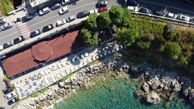 Vista dall'alto di un hotel ristorante sul mare a Scilla Calabria, Italia - Video drone mostra le rocce bagnate dal mare turchese cristallino e una attivit&agrave; turistica sotto il livello stradale