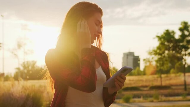 Young woman in red checkered shirt inserts earphones into the ear at sunlight 