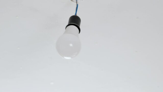 Swinging of an electrical energy saving light bulb on a wire due to shaking of the ceiling during an earthquake close up
