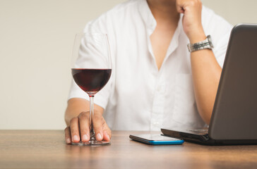 Businessman's right hand touches the base of a glass of red wine while sitting at the table