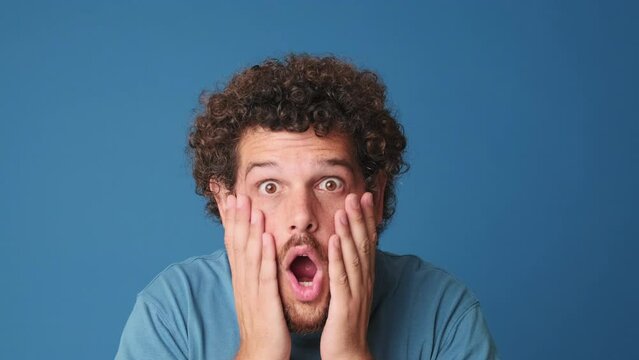 Close up, shocked man looking at the camera with big eyes, says wow, isolated on blue background 
