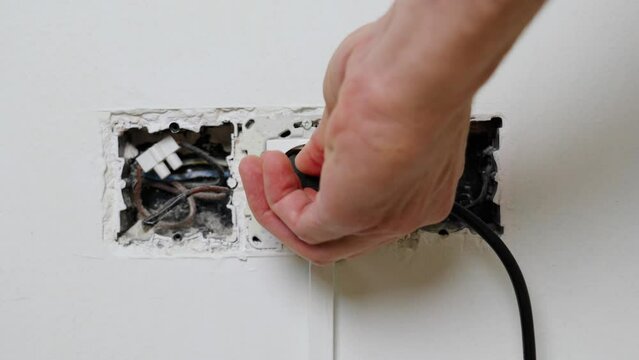 Unplugging an electrical plug from a broken defective damaged wall socket with uncovered wires close up