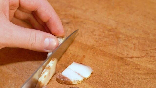 Slicing of salted pork fatback on cutting board, close-up