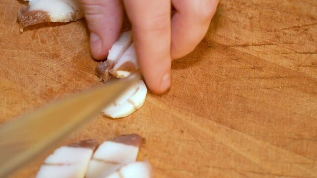 Slicing of salted pork fatback on cutting board, close-up