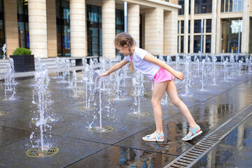 Active little girl playing with splash spray water. Happy kid in fountain in wet clothes. summer children pastime, entertainment, recreation. child's leisure, childhood in city