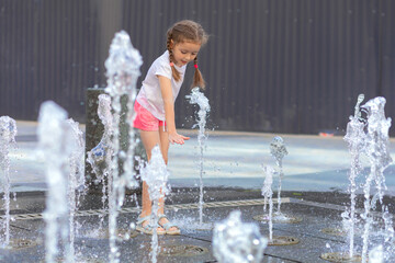 Active little girl playing with splash spray water. Happy kid in fountain in wet clothes. summer...