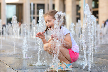 Active little girl playing with splash spray water. Happy kid in fountain in wet clothes. summer children pastime, entertainment, recreation. child's leisure, childhood in city