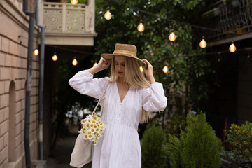 blonde in a white sundress dress with a bouquet of daisies. Walk around the city.
