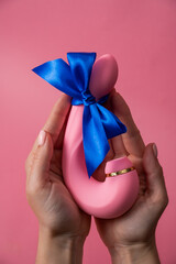 Woman holding curved dildo with blue ribbon on pink background. 